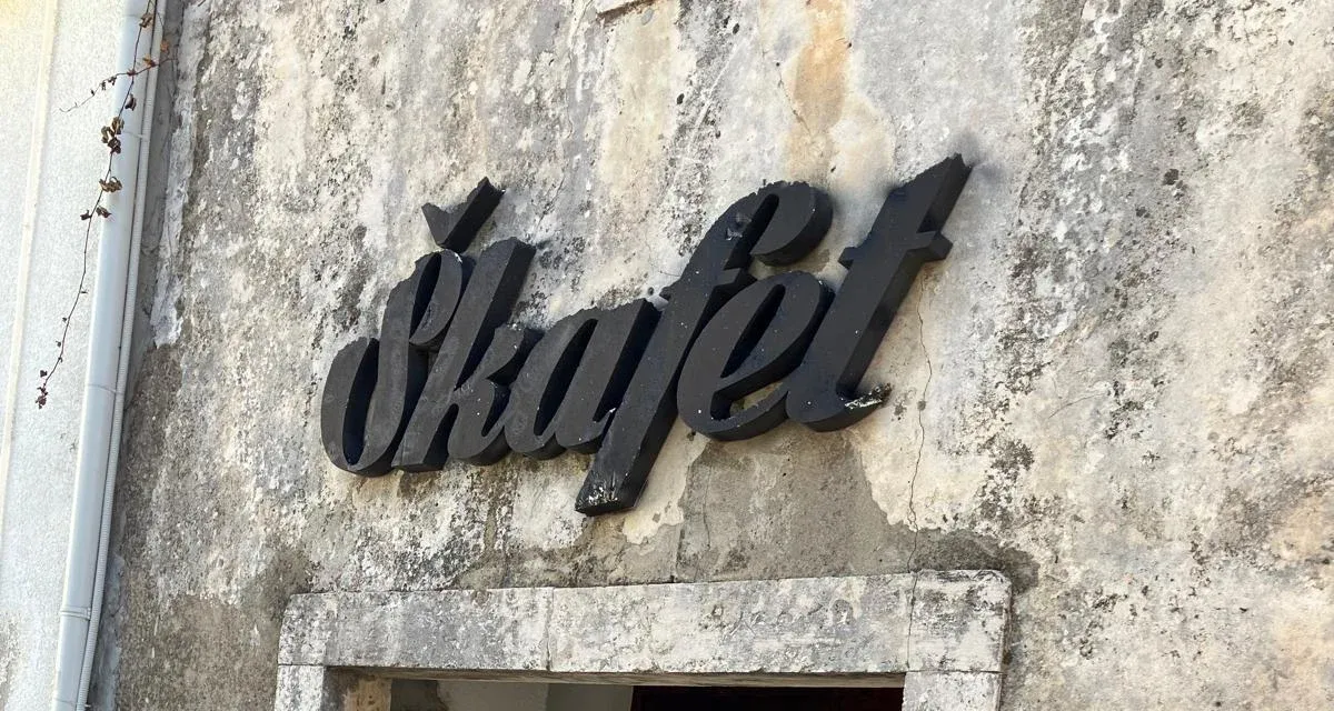 Nápis Škafet z černých písmen na staré omítnuté zdi nad kamenným rámem vchodu.